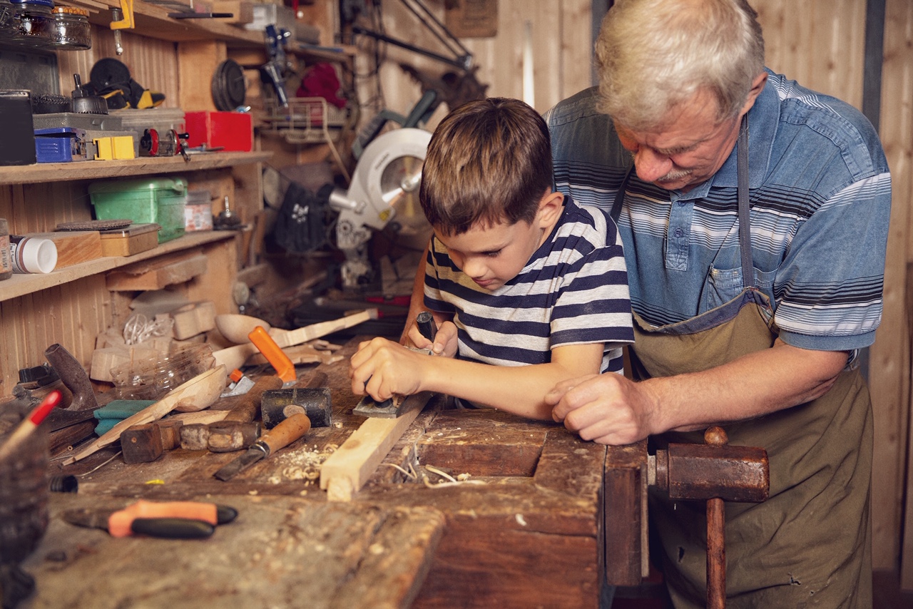 young carpenter working in a workshop. grandfather teaches grandson to work with a jack plane